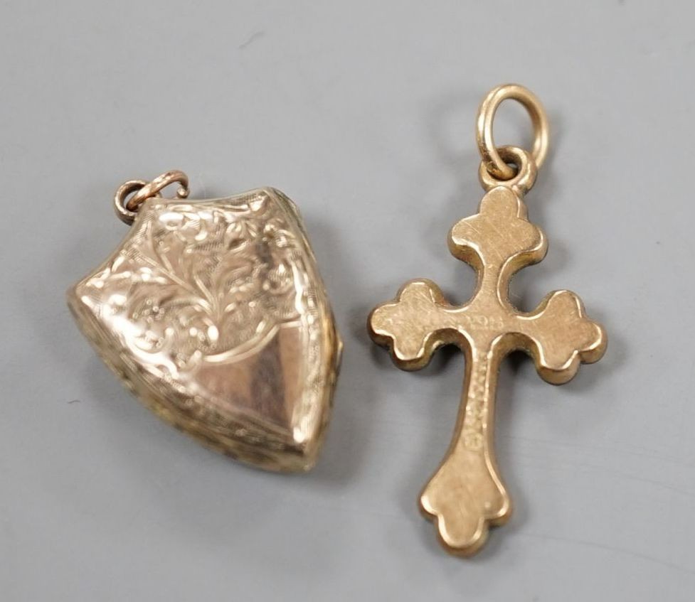 A 9ct gold cross pendant charm, 21mm and a similar engraved yellow metal shield shaped locket charm